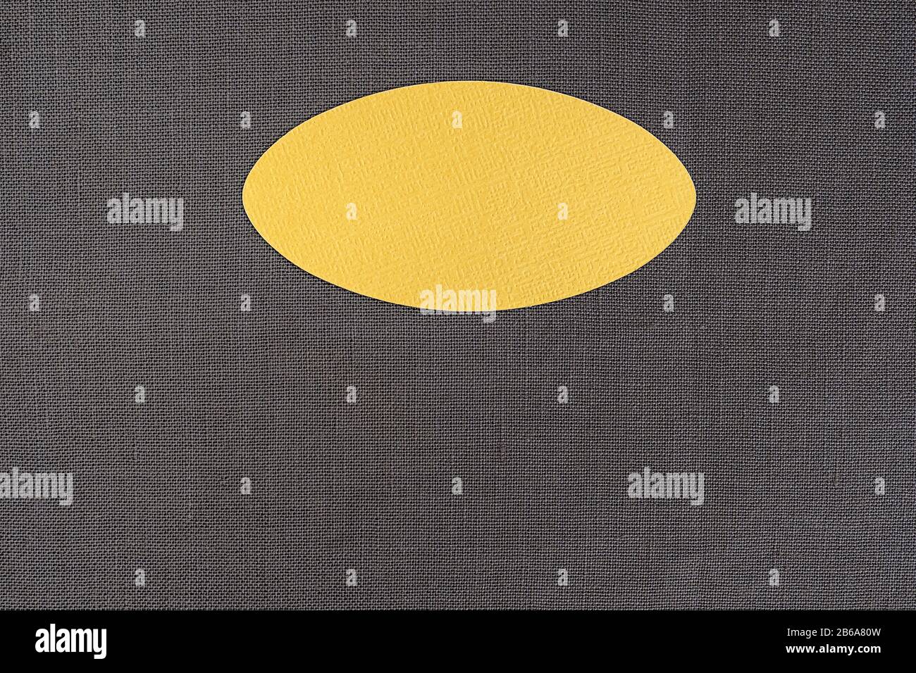 taglio ovale di un cartoncino fotografico giallo per l'etichettatura su tessuto di cotone scuro Foto Stock