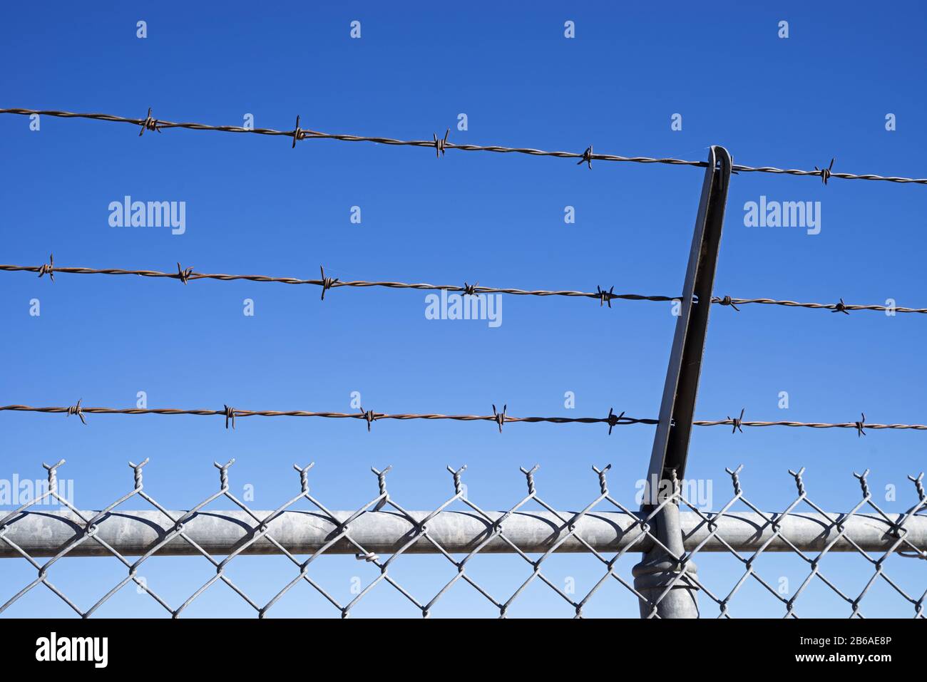 filo spinato angolato sulla parte superiore di una recinzione di maglia di catena con sfondo blu cielo Foto Stock