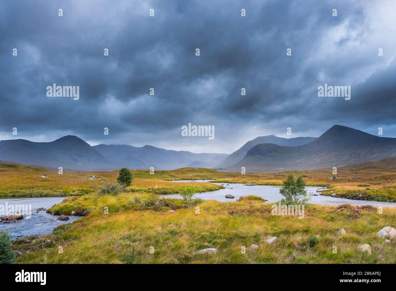 Colline sotto un cielo tempestoso con un flusso tortuoso in primo piano. Scottish Highlands, Regno Unito Foto Stock