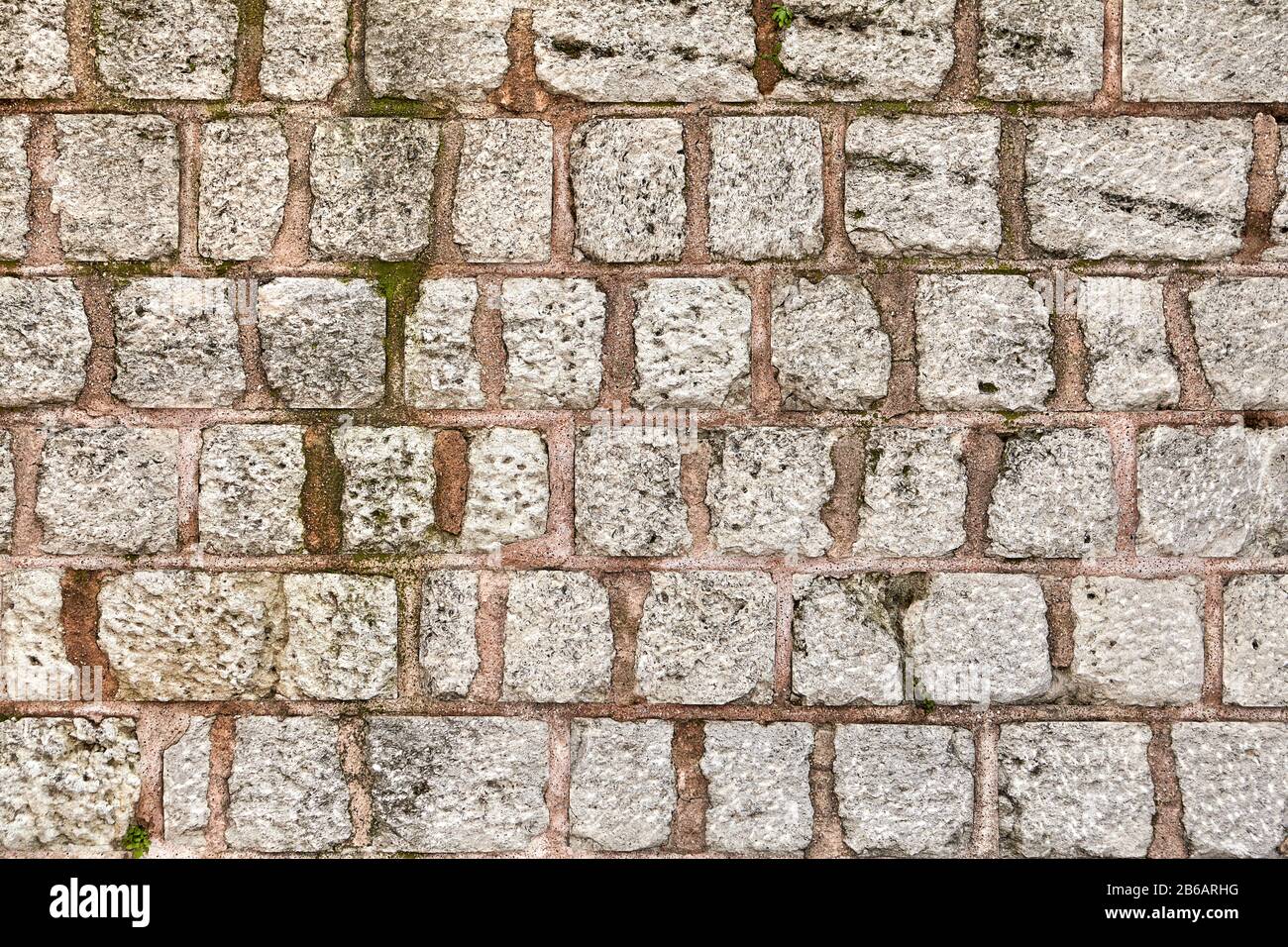 La superficie della parete è in acciottolato grigio fissato con una soluzione di argilla rossa. Trama di una recinzione in pietra per lo sfondo. Foto Stock
