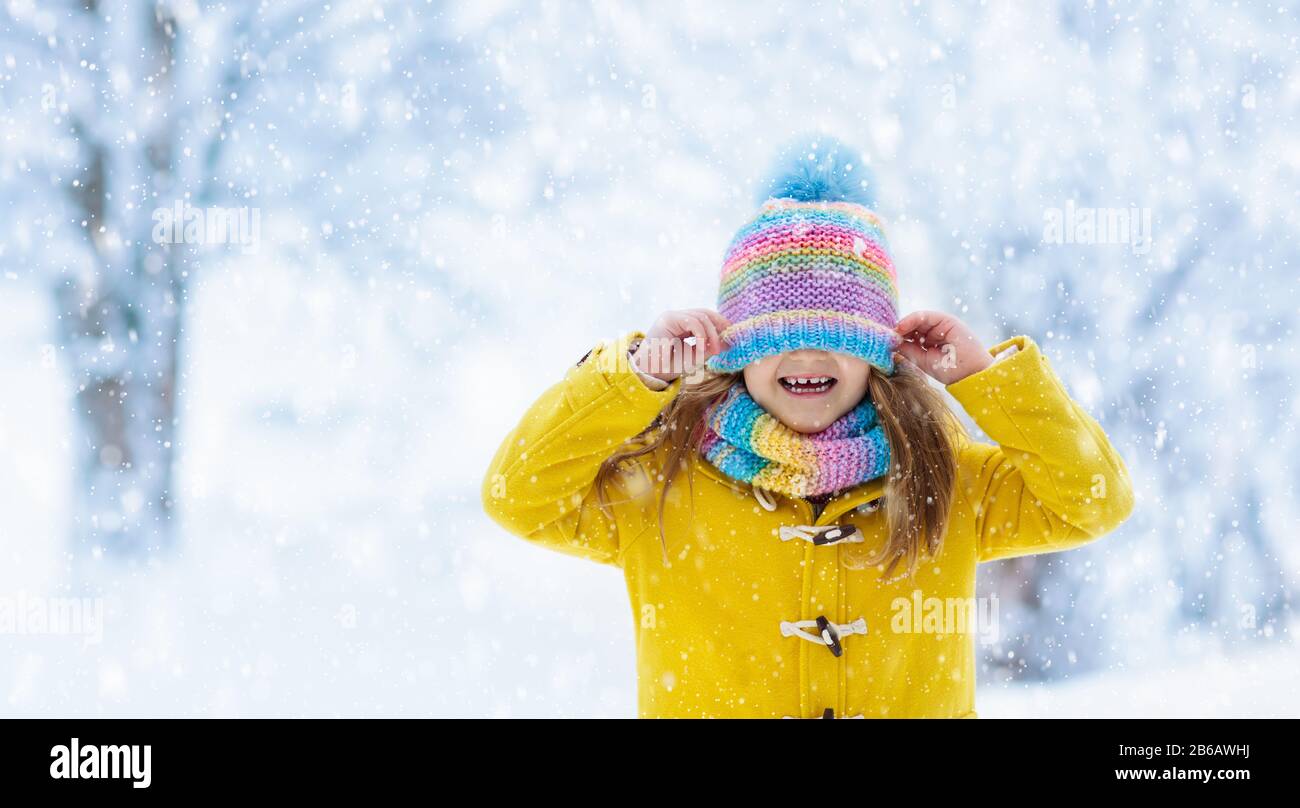 Bambino in maglia hat giocare nella neve sulle vacanze di Natale. Inverno di divertimento all'aperto. La maglieria e capispalla per famiglia. I bambini giocano nel parco innevato. Poco gir Foto Stock