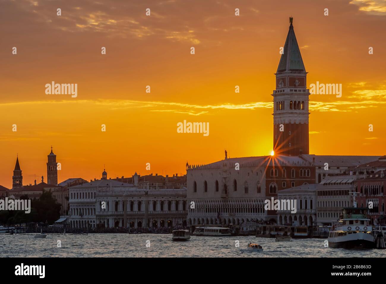 Tramonto colorato sul centro storico di Venezia, Italia, con raggi di sole che filtrano dal Campanile di San Marco sopra il Palazzo Ducale Foto Stock