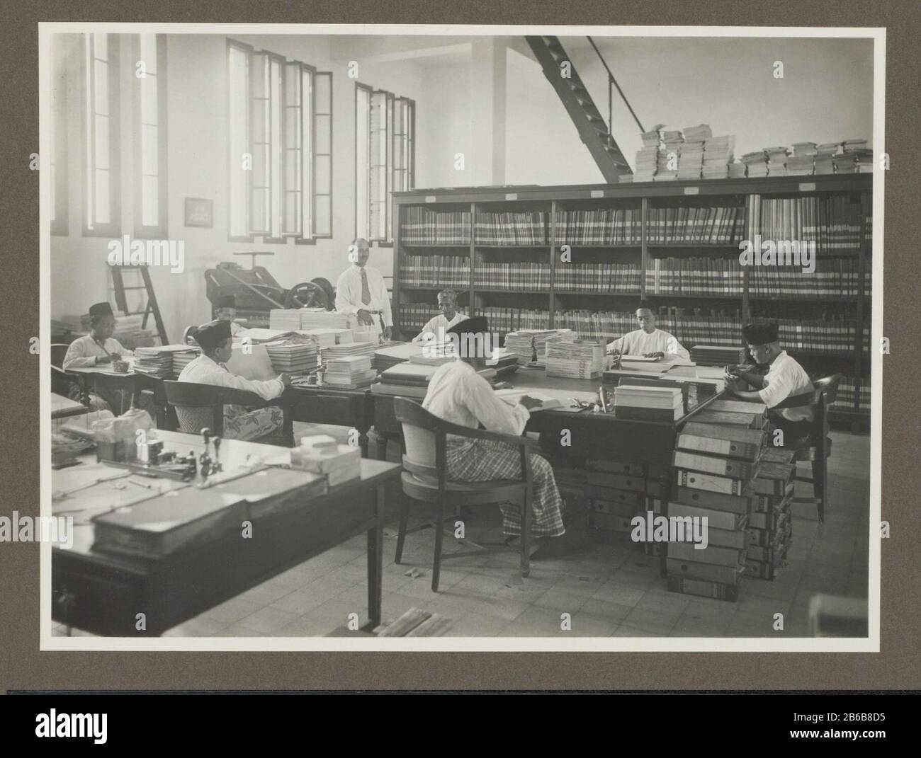 Archivio (oggetto del titolo) l'archivio dei lavoratori giavanesi seduti ai tavoli tra pile di documenti e cartelle. Foto nella galleria offerta a A. van der Eyk per conto degli chef e dello staff della Trade Association Amsterdam (HVA) a Surabaya alla sua partenza da Java nell'aprile 1931. Produttore : fotografo: Atelier KurkdjianPlats produce Surabaya Data: Apr 1931 caratteristiche Fisiche : gelatina argento materiale di stampa: Carta Tecnica: Gelatina argento dimensioni di stampa: Foto: H 170 mm × W 230 mm Data: 1920 - 1931 Foto Stock