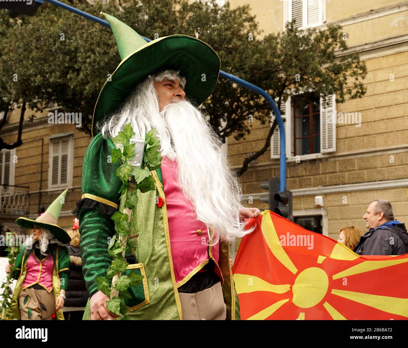 Rijeka, Croazia, Febbraio 23rd, 2020. Bandiera della Macedonia del Nord nella mano di un uomo mascherato come un elfo o mago con barba bianca su una processione carnevale Foto Stock