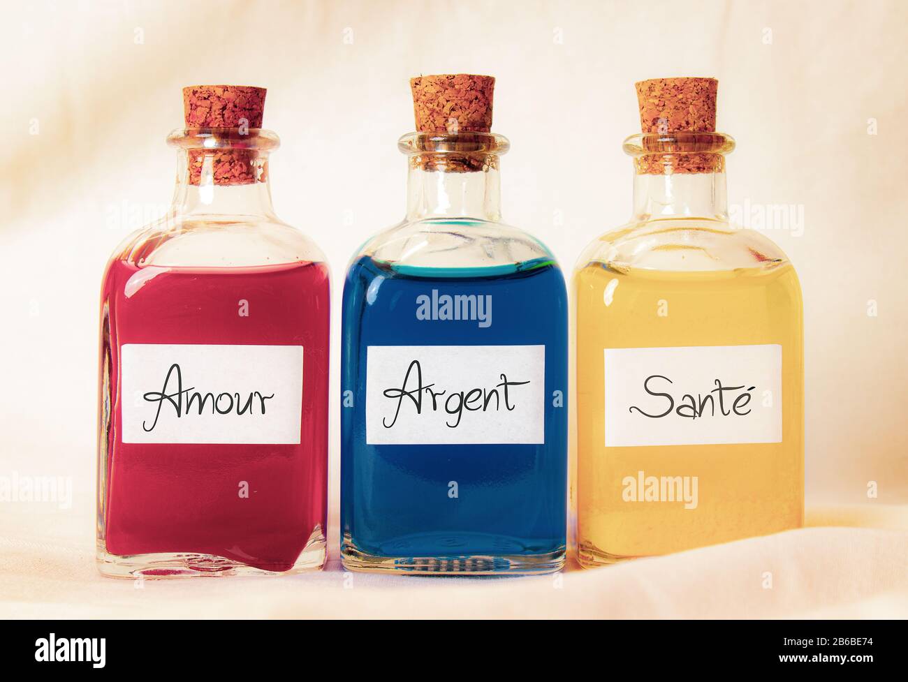 Tre bottiglie di vetro rosso blu e giallo con le parole Amour Argent Sante scritta in francese. Le bottiglie utilizzano un conduttore di sughero e lo sfondo è bianco Foto Stock