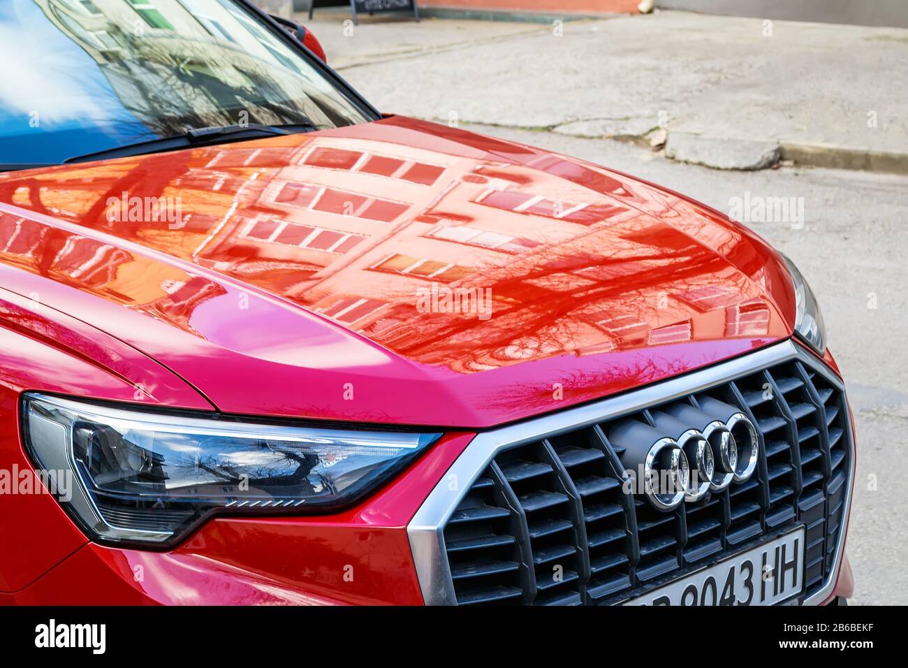 Varna, Bulgaria, 28 Dicembre 2019. Griglia Audi per auto con logo cromato e cofano anteriore con riflessi di edifici residenziali. Auto rossa parcheggiata su una stree Foto Stock