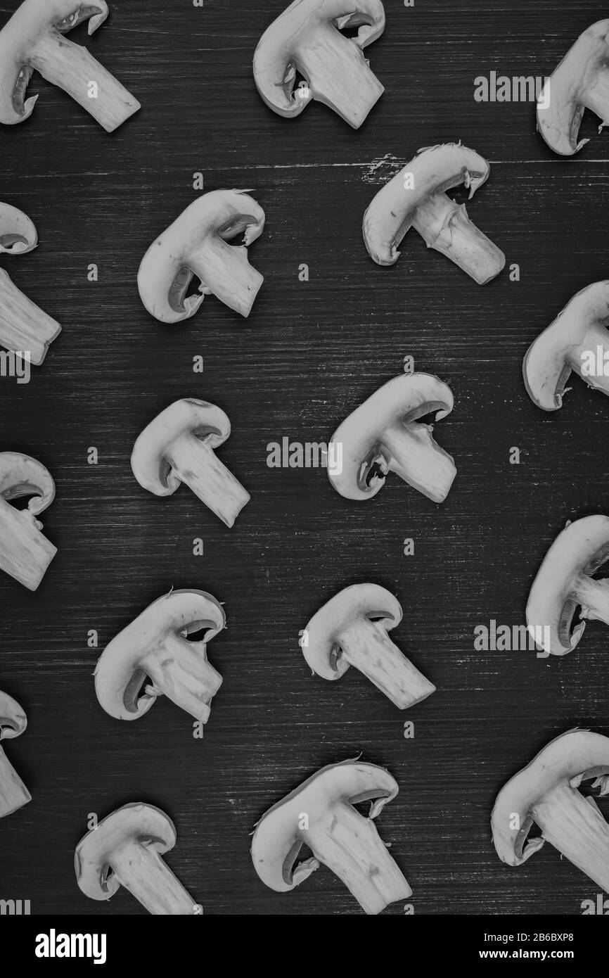 Funghi a fette bianche su sfondo rustico in legno nero, immagine monocromatica. Disposizione piatta di campaignoni bianchi sul tavolo Foto Stock