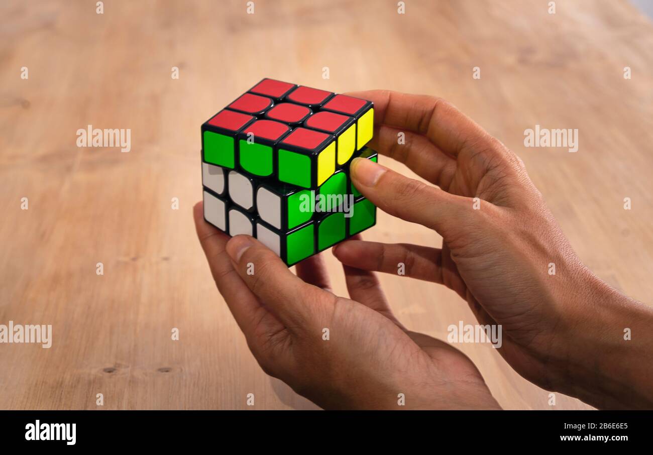 Cubo di Rubik intelligence toy risolvendo in una mano in una tavola di legno Foto Stock