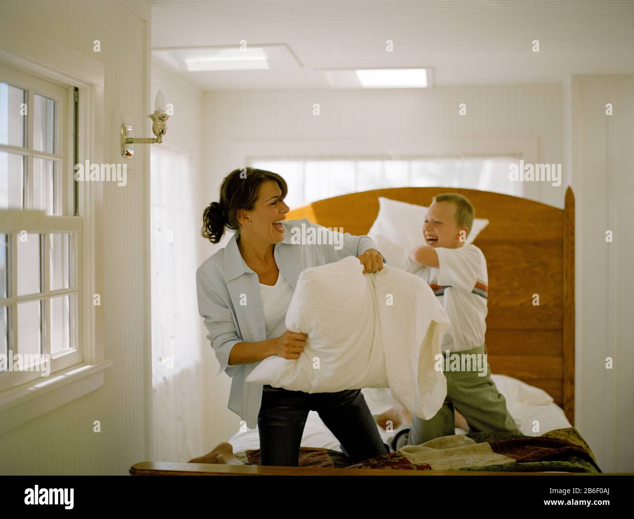 Donna matura avente lotta di cuscini sul letto con suo figlio. Foto Stock