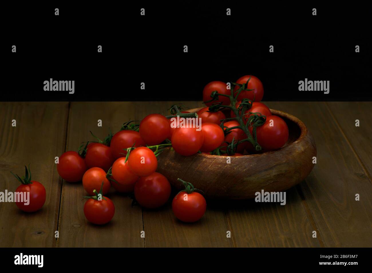 Pomodori ciliegini freschi su sfondo nero visto dal lato, Fresco intero e tagliato (dimezzato) rosso tomatillos su sfondo nero visto dall'alto – fo Foto Stock