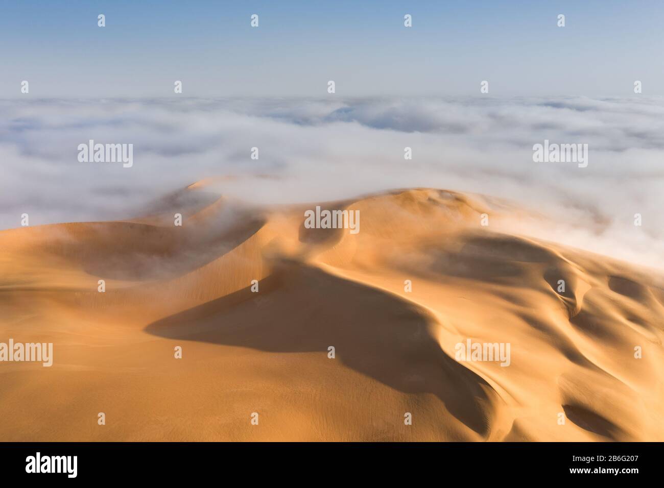 Cima di una gigantesca duna di sabbia che emerge da una fitta nube di nebbia dopo l'alba. Liwa Desert, Abu Dhabi, Gli Emirati Arabi Uniti. Foto Stock