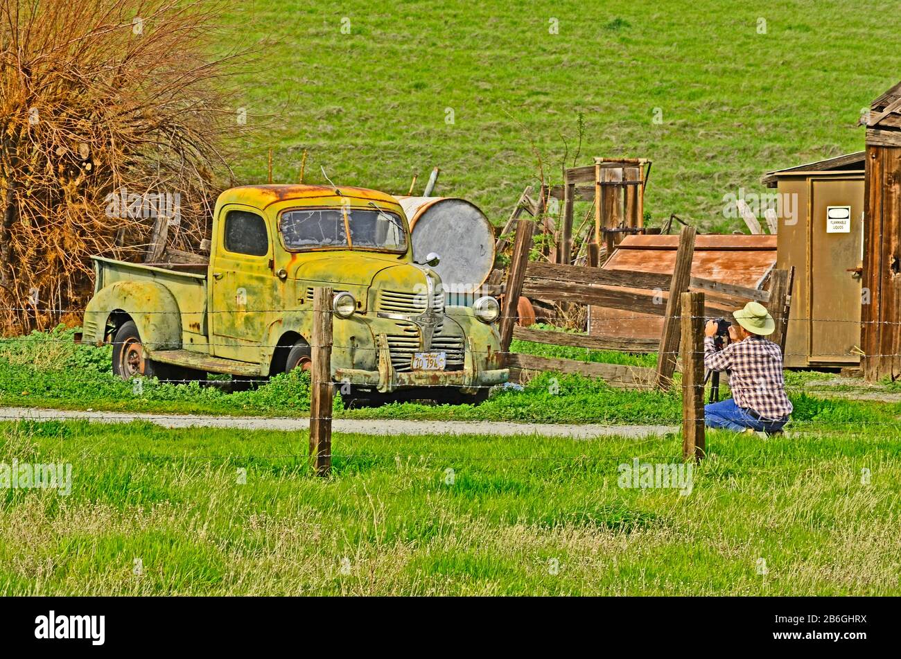 Il fotografo che indossa una maglietta con plaid, cappello e jeans si prepara a fotografare un camion verde arrugginito, il Black Diamond Regional Park, Antioch, California, USA Foto Stock