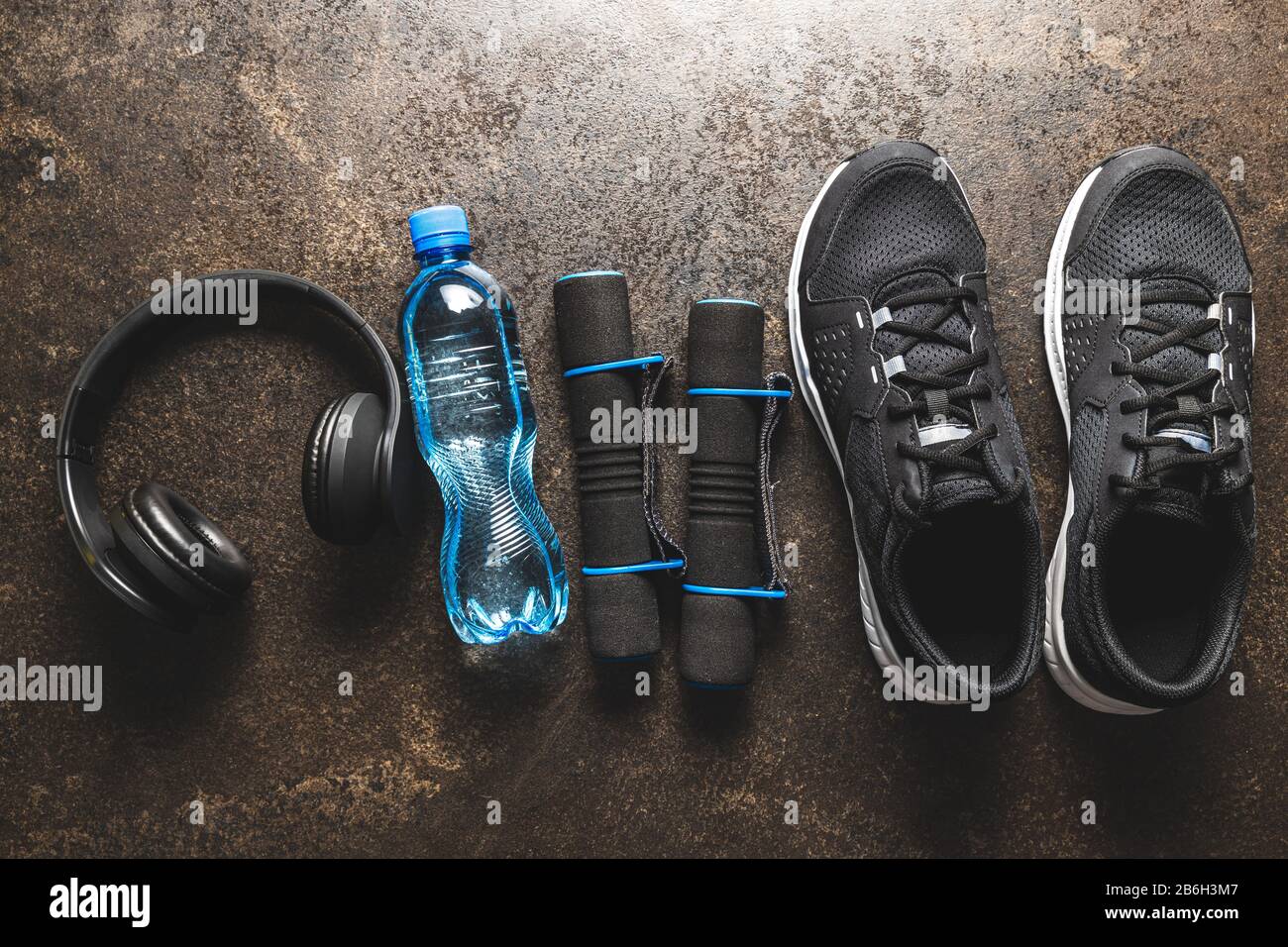 Concetto di fitness. Scarpe sportive nere, testofoni, dumbbell e bottiglia d'acqua sul vecchio tavolo. Vista dall'alto. Foto Stock