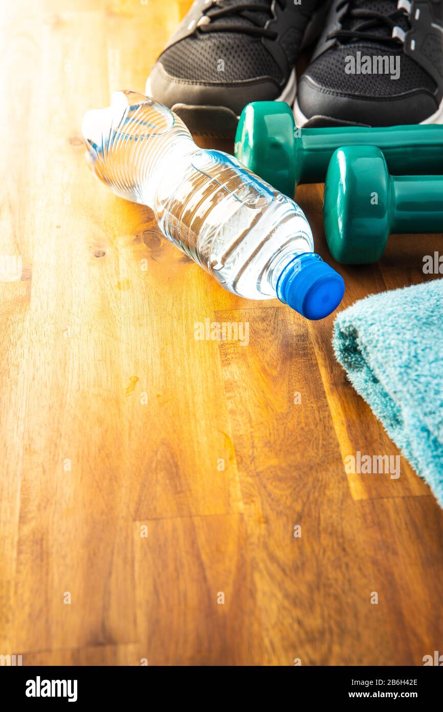 Concetto di fitness. Scarpe sportive nere, manubrio e bottiglia d'acqua su pavimento in legno. Foto Stock