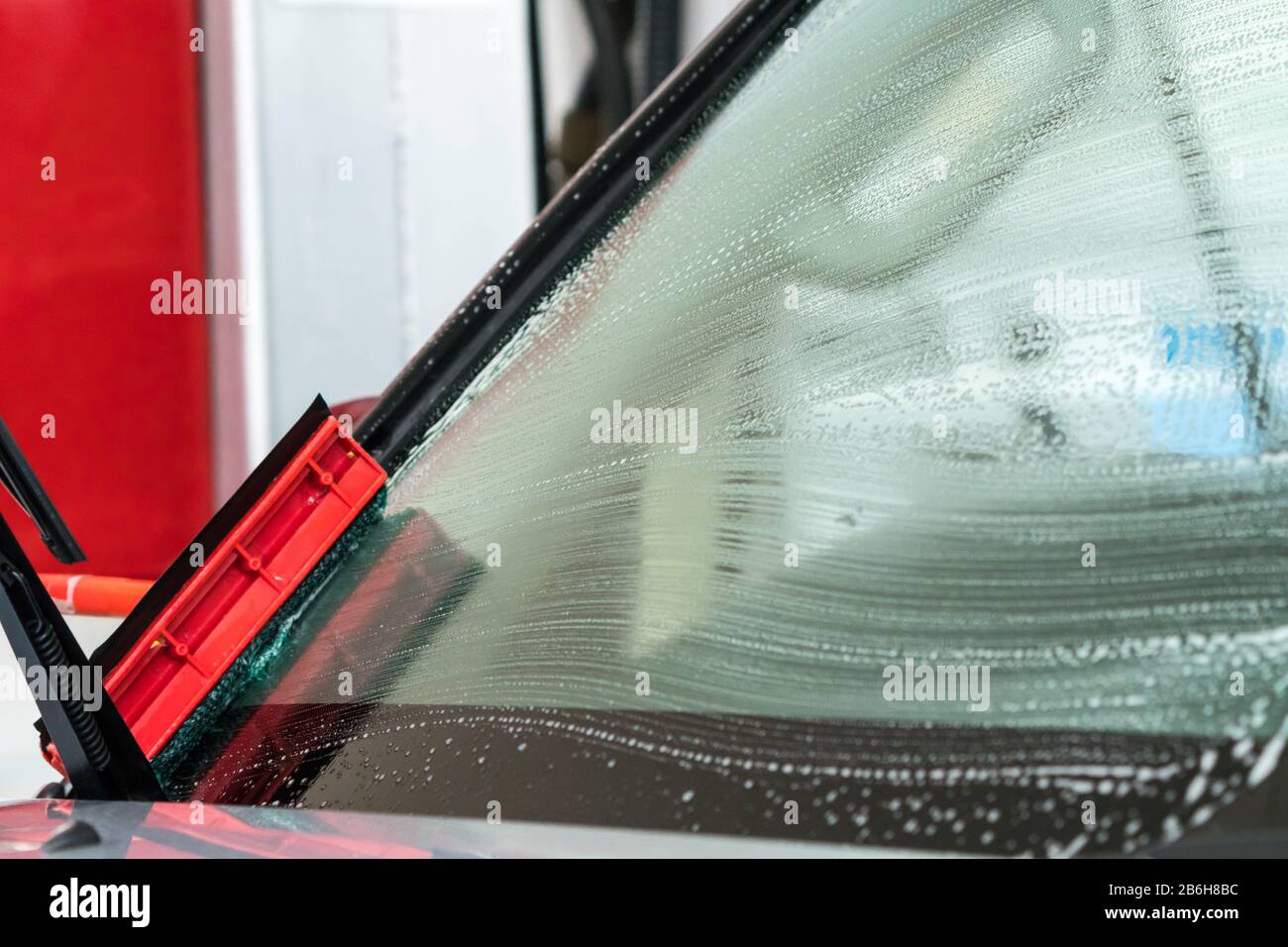 pulire o lavare un parabrezza per auto, con tracce di bolle di sapone sulla superficie del vetro Foto Stock