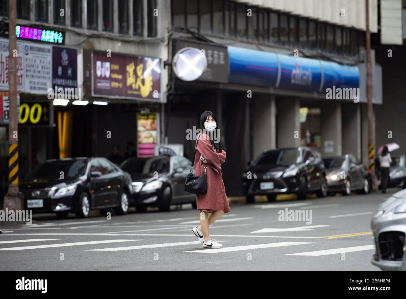 Una ragazza cinese, indossando una maschera facciale per proteggersi dal nuovo coronavirus (2019-nCoV) o (COVID-19) sta attraversando un incrocio a Taipei. Foto Stock