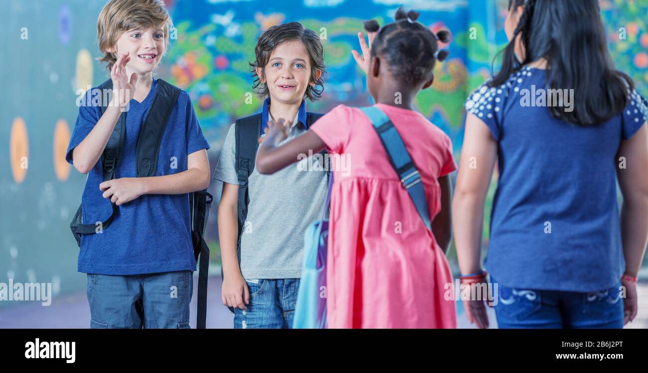 Multi etnico classe elementare I bambini si salutano nel cortile della scuola. Foto Stock