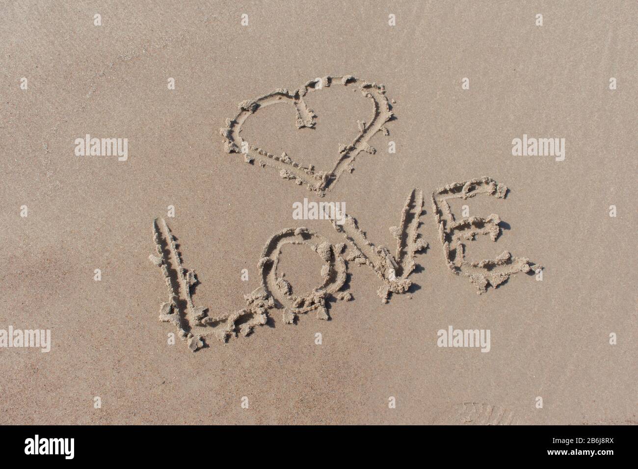 Simbolo di cuore disegnato e amore di parola scritto nella sabbia della spiaggia Foto Stock