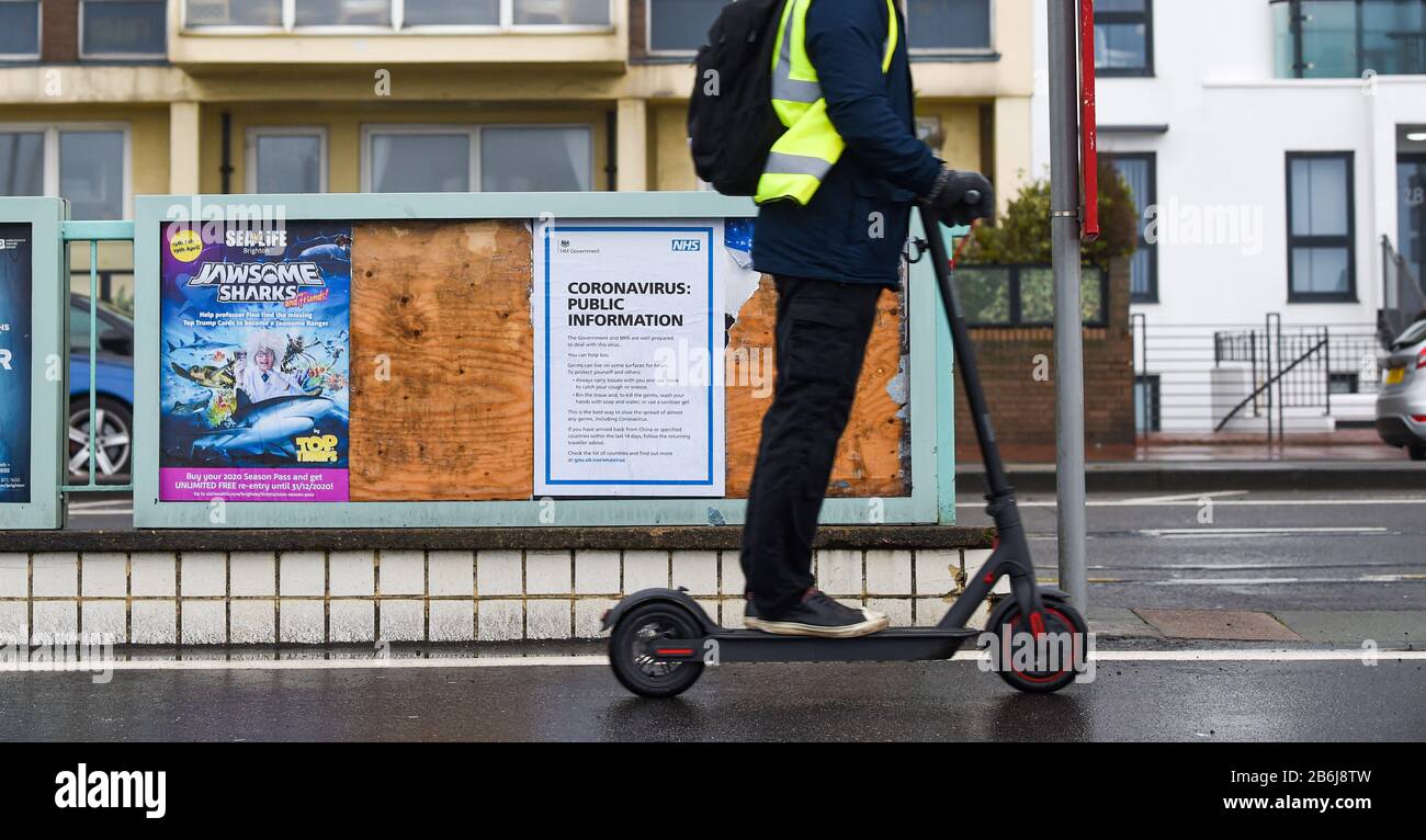 Brighton UK 11th March 2020 - un pendolari di mattina presto su uno scooter elettrico passa da un NHS Coronavirus informazione sul lungomare di Brighton . Credito: Simon Dack / Alamy Live News Foto Stock