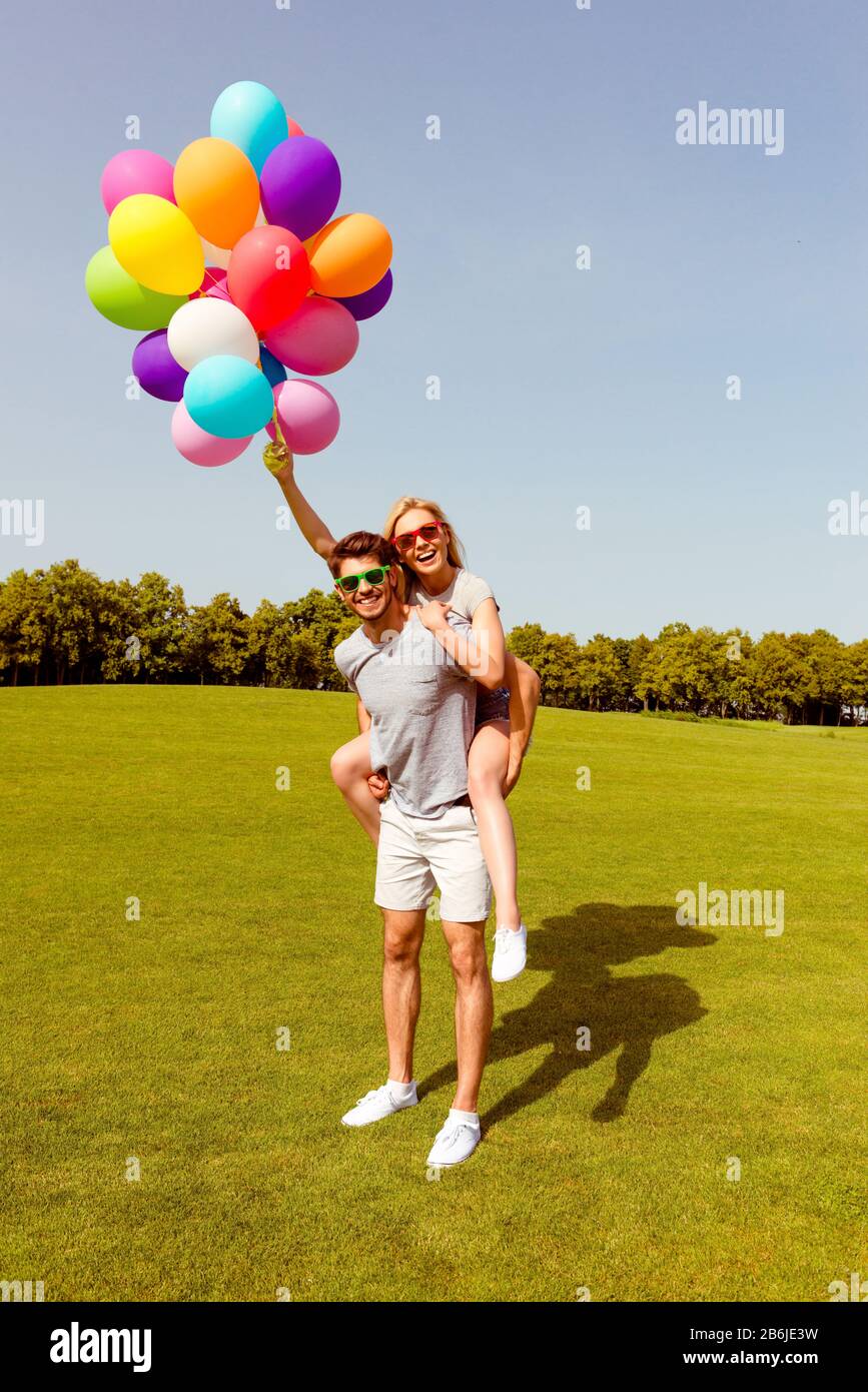 Felice ragazzo giovane piggybacking la sua ragazza allegra con palloncini Foto Stock