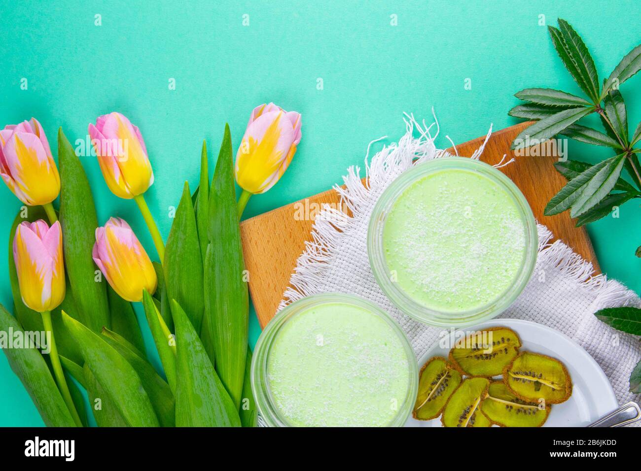Yogurt di limone alla menta con kiwi in ciotole per insalata su una tavola di legno con tulipani su uno sfondo rosa Foto Stock