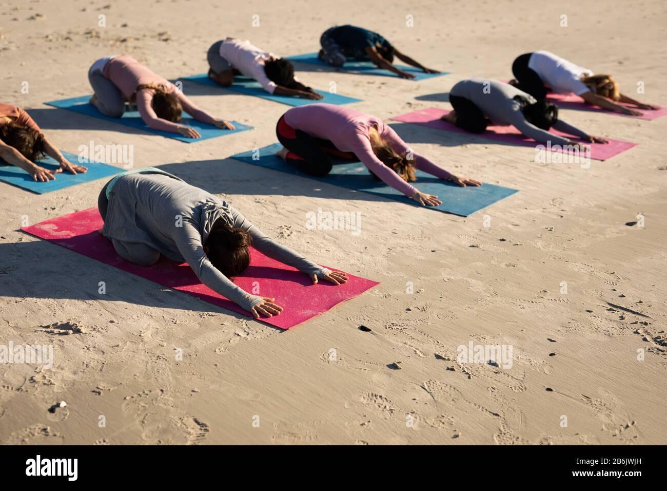 Vista laterale delle donne che appoggiano sui tappetini per lo yoga sulla spiaggia Foto Stock