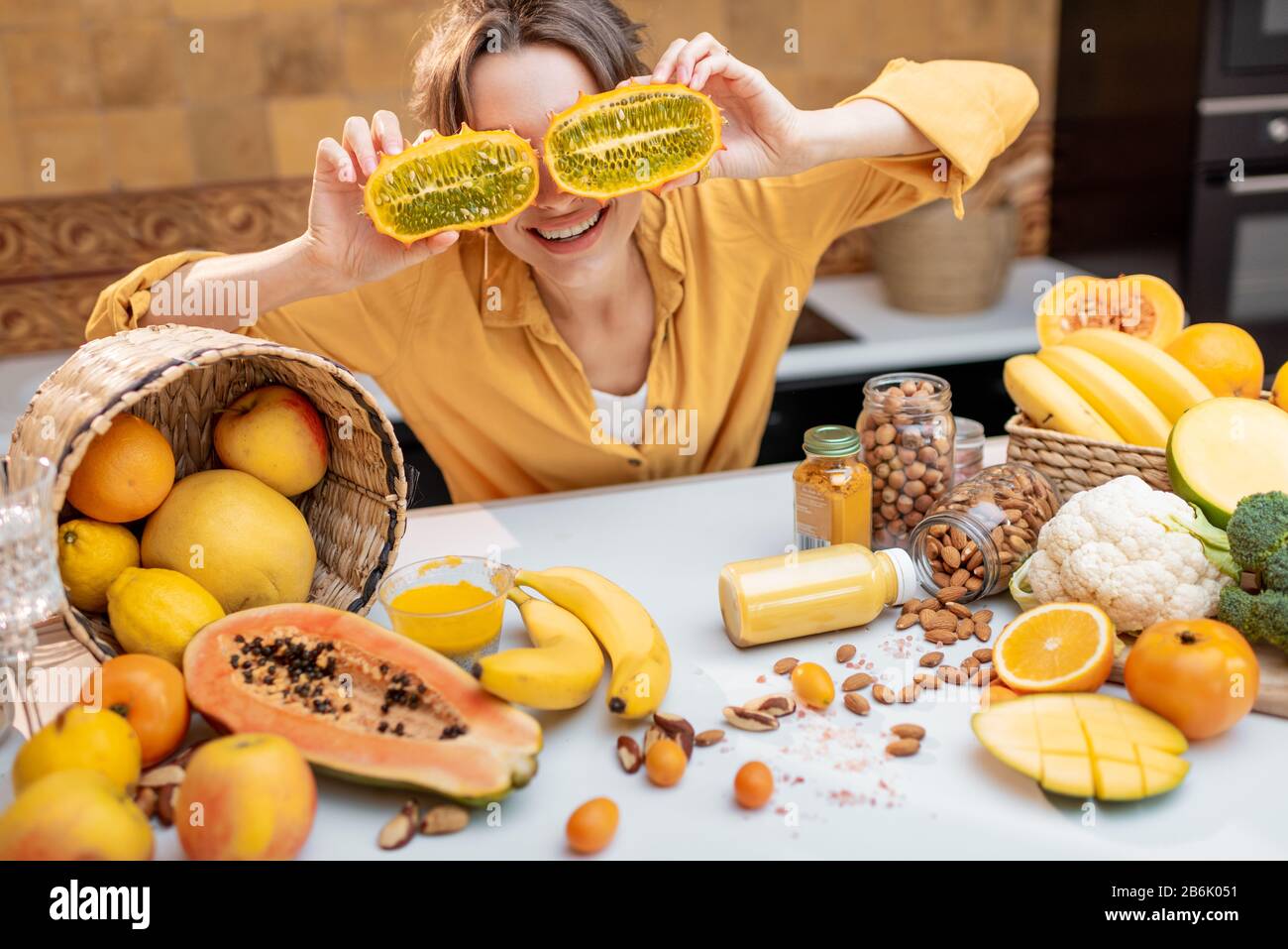 Ritratto di una donna gioiosa con varietà di frutta esotica e verdure in cucina, tenendo a fette il cetriis metuliferus. Concetto di vegetarianismo e di alimentazione sana Foto Stock