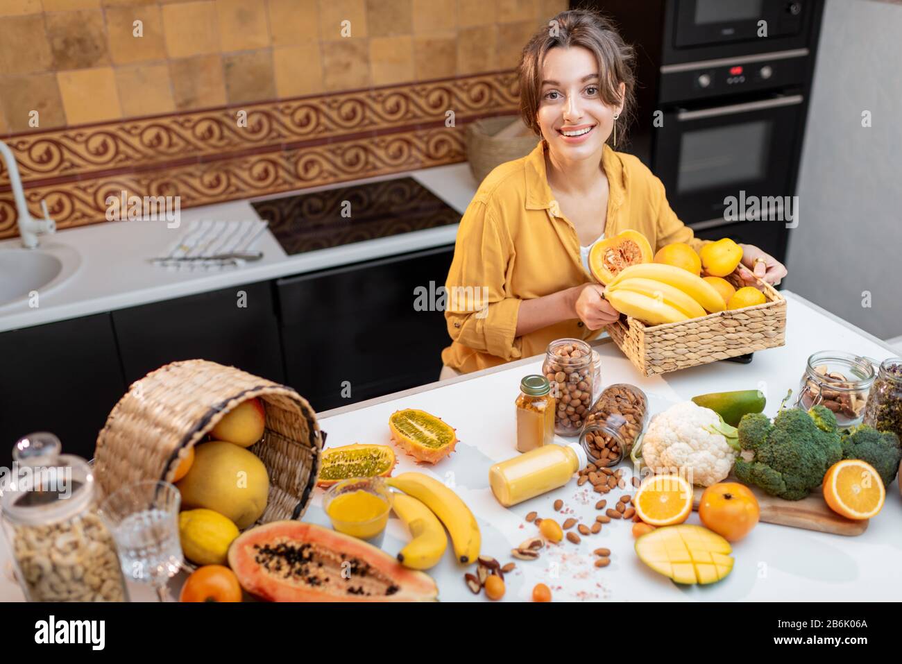Giovane e allegra donna che cucina con una varietà di verdure fresche e frutta la cucina a casa. Mangiare cibo fresco sano concetto Foto Stock