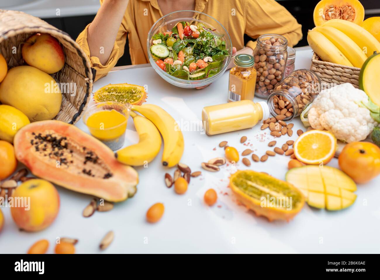 Donna che mangia insalata al tavolo pieno di verdure sane crude e frutta, vista tagliata senza faccia. Concetto di vegetarianismo, sano mangiare e benessere Foto Stock