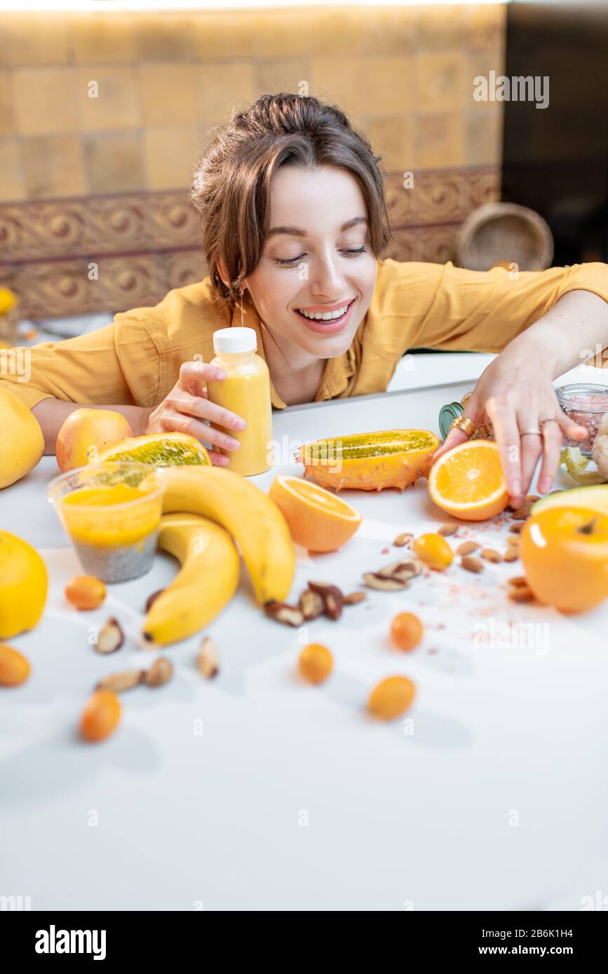 Ritratto di una giovane e gioiosa donna che tiene una bottiglia di succo al tavolo pieno di sane verdure crude e frutta. Concetto di vegetarianismo, detox, sano mangiare e benessere Foto Stock