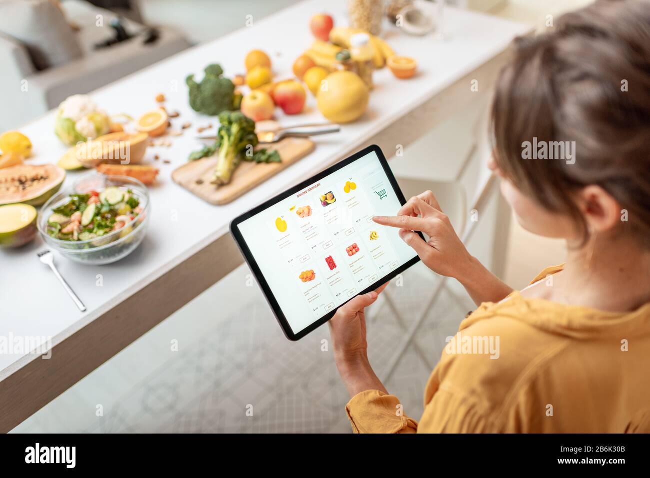 Donna che acquista cibo online utilizzando un tablet digitale in cucina. Concetto di acquisto online tramite dispositivi mobili Foto Stock