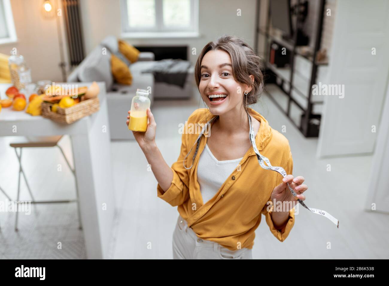 Ritratto di una giovane e allegra donna con succo e metro a nastro a casa. Perdita di peso e sano concetto di consumo Foto Stock