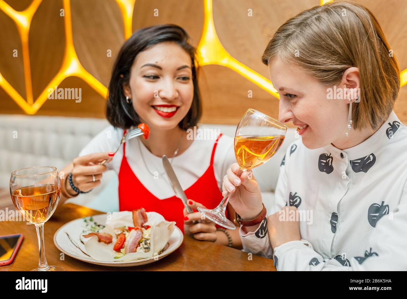 Due amici femminili Bevono vino e si gustano i pasti al ristorante Foto Stock