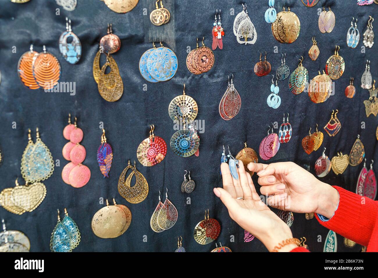 Donna cliente scegliendo tra molti colorati orecchini fatti a mano in vendita alla fiera del mercato Foto Stock