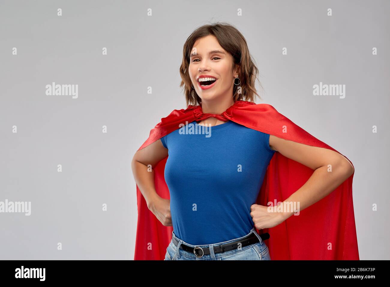 concetto di potere e di gente delle donne - donna felice in capo supereroe rosso su sfondo grigio Foto Stock
