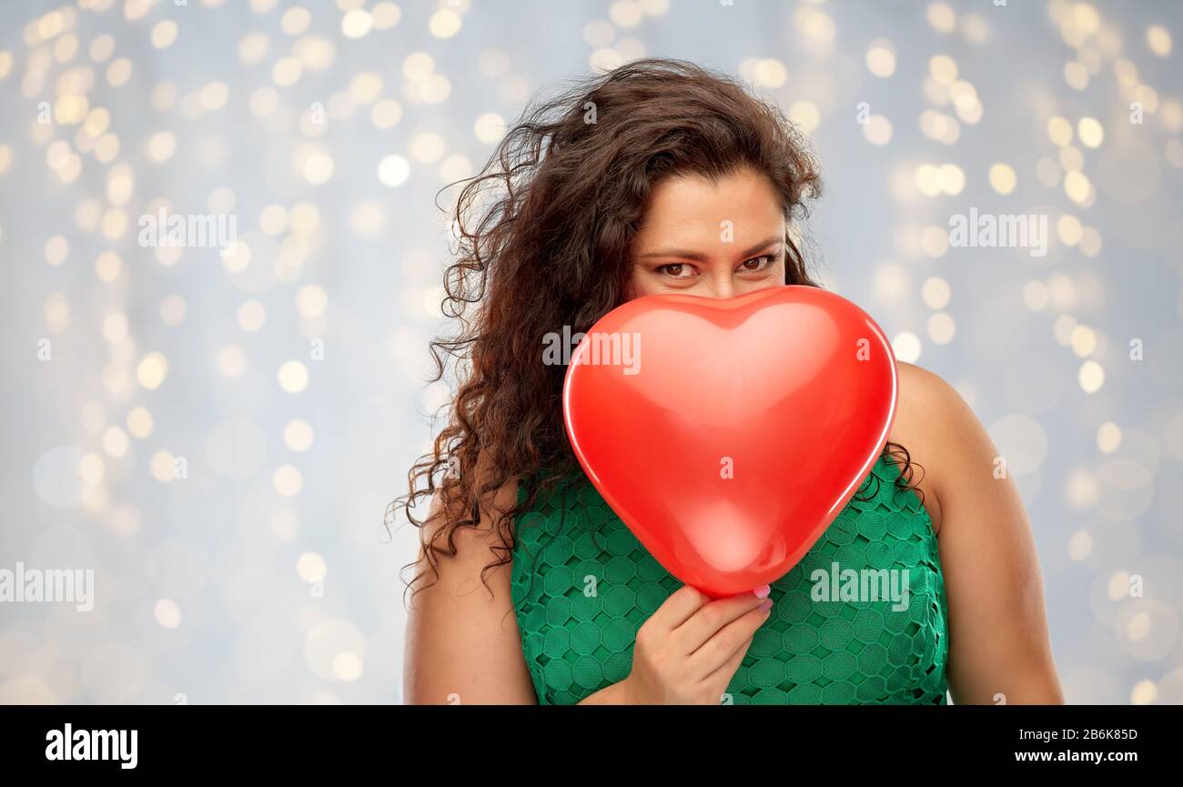 san valentino, vacanze e amore concetto - donna giocosa in abito verde nascosto dietro il cuore rosso palloncino a forma di cuore sulle luci di festa sul backgroun grigio Foto Stock
