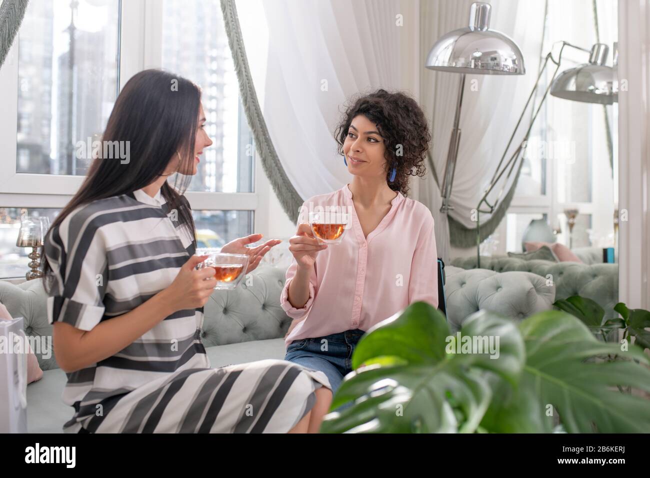 Due donne dai capelli scuri che si siedono in un salone di bellezza e hanno il tè Foto Stock