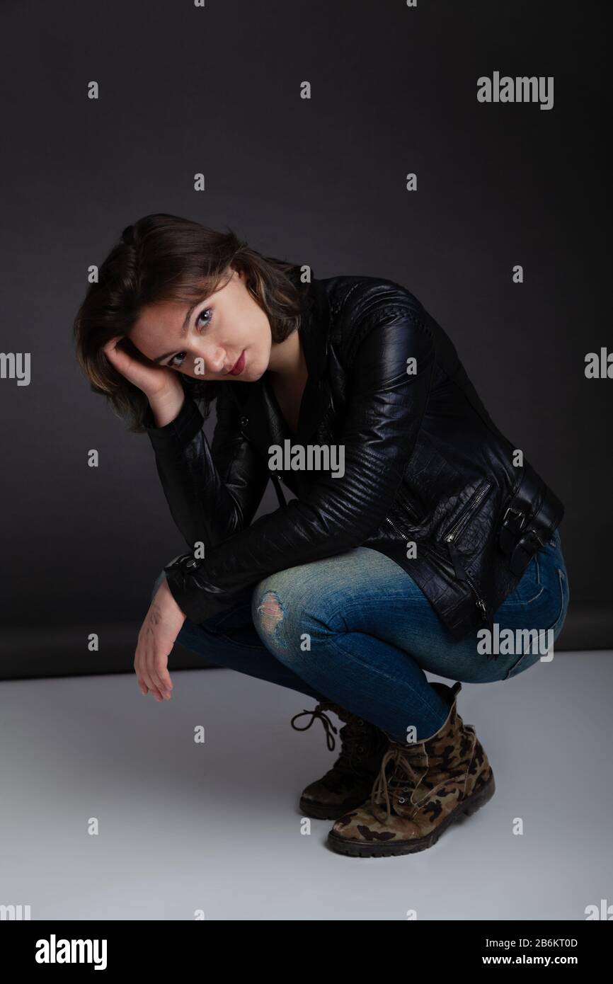 Donna di venti anni accovacciata indossando un lungo ponticello con maniche e jeans blu. Foto Stock