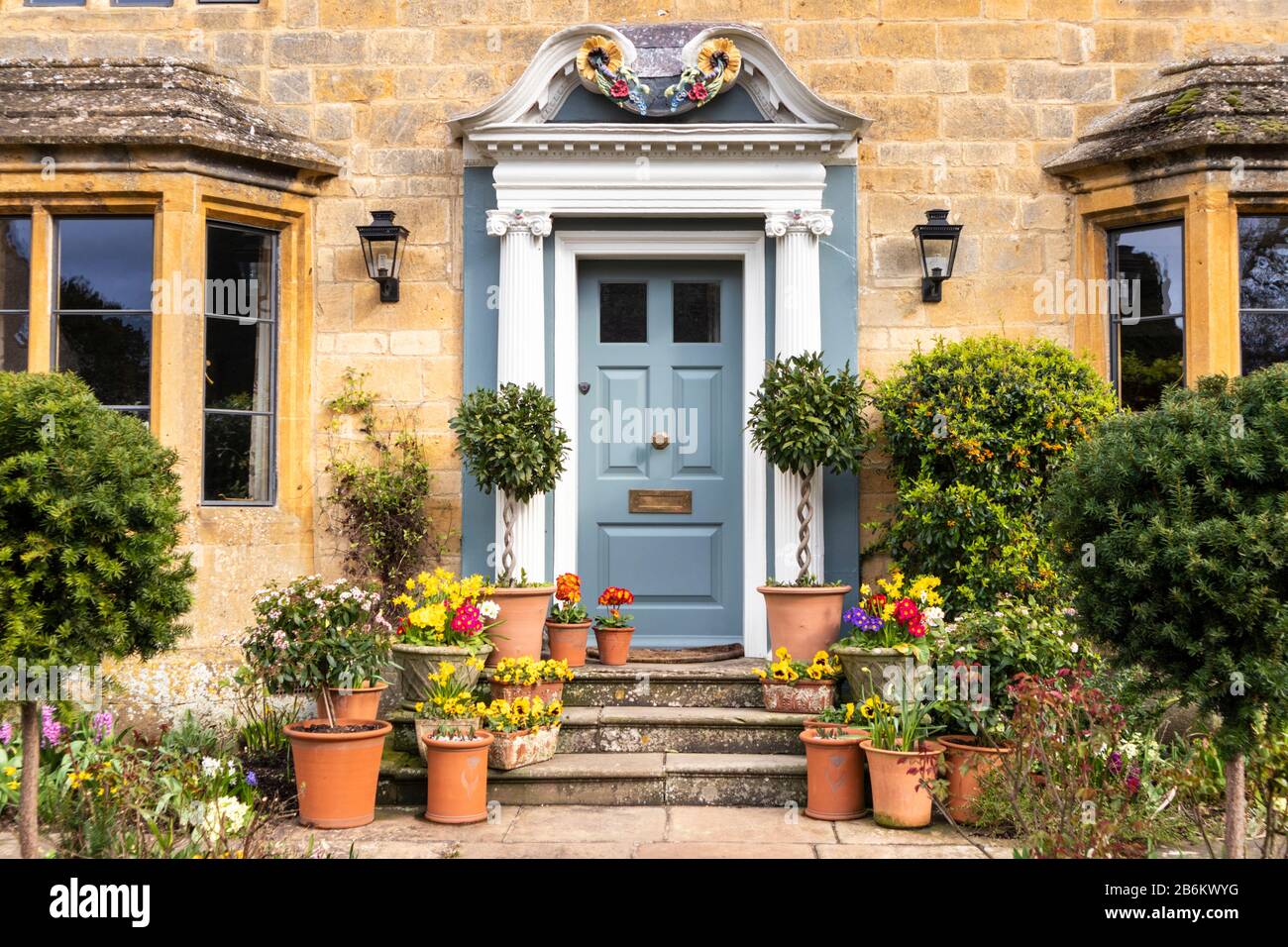 Una mostra di fiori primaverili in vasi fuori di una casa di pietra nel villaggio di Cotswold di Broadway, Worcestershire UK Foto Stock