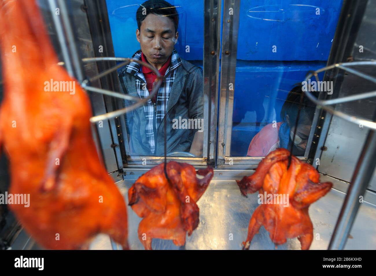 20.12.2013, Yangon, Repubblica dell'Unione di Myanmar, Asia - un uomo si trova dietro la sua strada stalla con polli alla griglia su una strada. Foto Stock