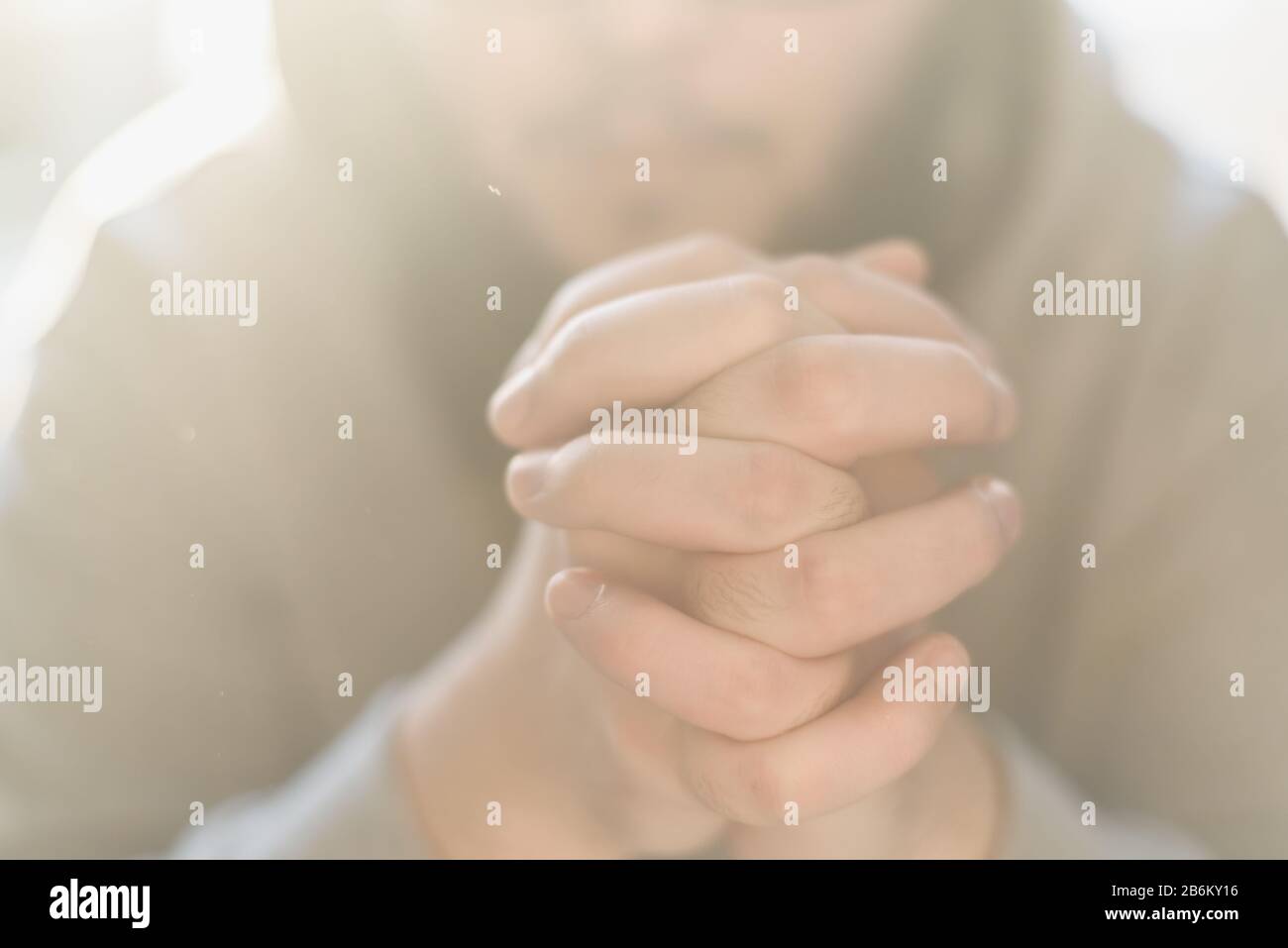 Uomo adulto bearded che prega a Dio che siede a casa nel raggio del sole. Un musulmano o cristiano alza le mani a Dio. Mani incrociate nel gesto di preghiera da vicino. Foto Stock