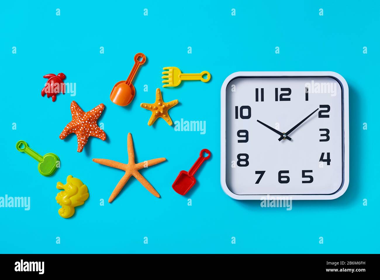 vista ad alto angolo di un orologio, alcune stelle marine e alcuni giocattoli da spiaggia diversi, come pale giocattolo e racchette, e alcuni diversi stampi di sabbia di diverso Foto Stock