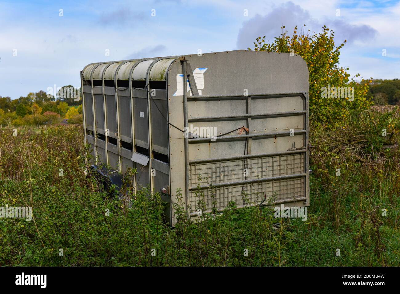 Rimorchio di scorta inutilizzato in un campo con arbusti ed erbacce che crescono intorno esso. Foto Stock
