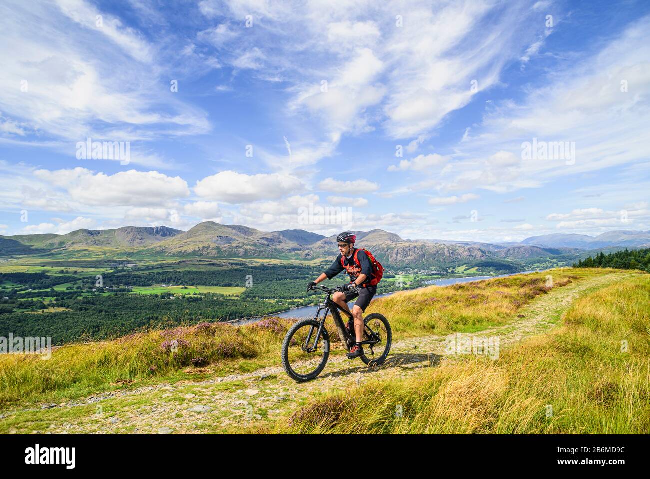 Ciclista (in bicicletta elettrica) sul crinale di Park Crags, con Coniston Water e le Coniston Fells dietro, nel Distretto dei Laghi Inglese Foto Stock