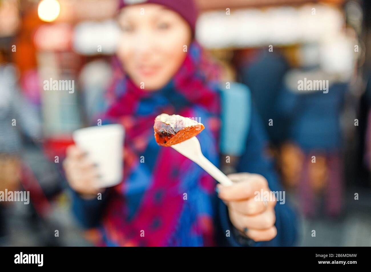 Donna che mangia salsiccia con vino caldo sulla piazza centrale della città europea. Concetto di Street food in inverno vicino alle attrazioni turistiche Foto Stock