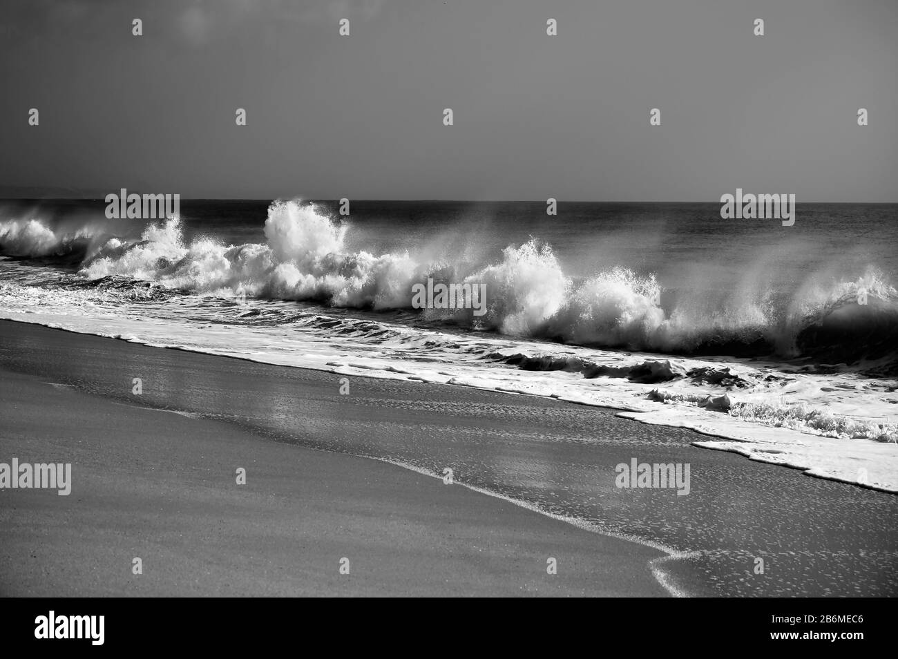 Vento attraverso le onde che si infrangono raggiungono la spiaggia. Fotografia in bianco e nero. Foto Stock
