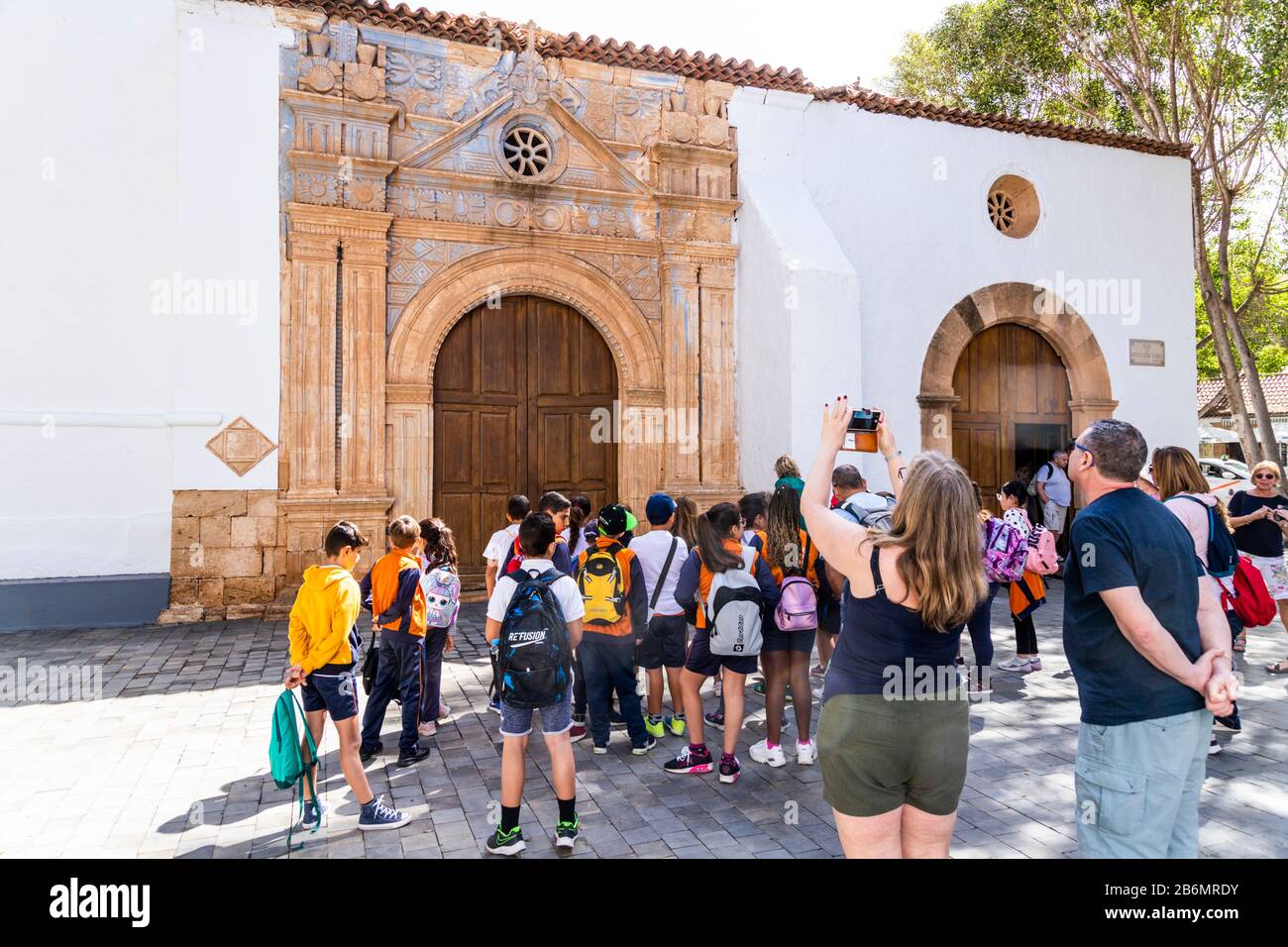 Un gruppo scolastico e turisti che ammirano l'intaglio con influenze azteche sulla chiesa di Iglesia Nuestra Senora de la Regla a Pajara sulle isole Canarie Foto Stock