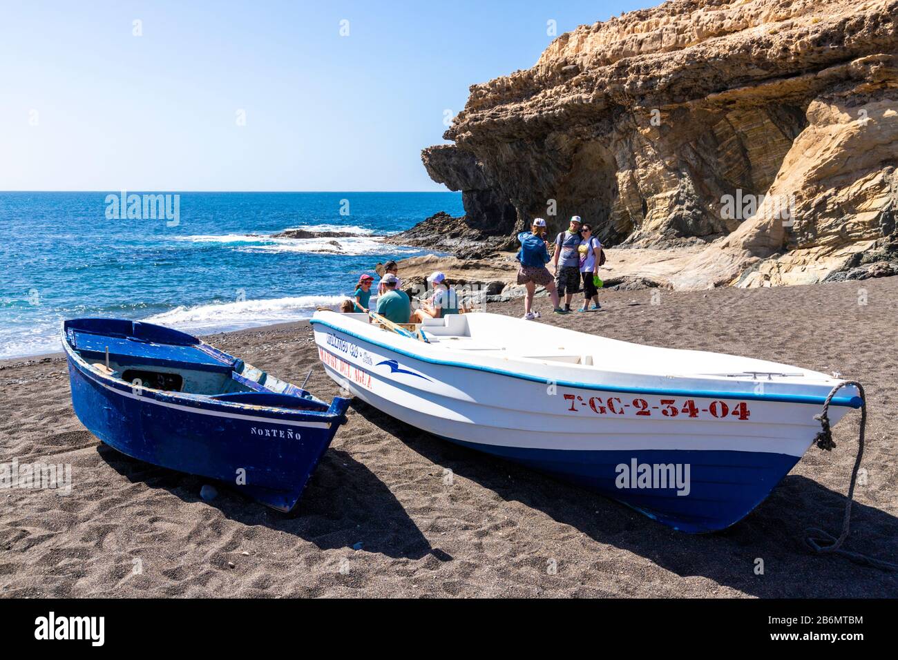 Barche da pesca e turisti sulla spiaggia di Ajuy sulla costa occidentale dell'isola delle Canarie di Fuerteventura Foto Stock