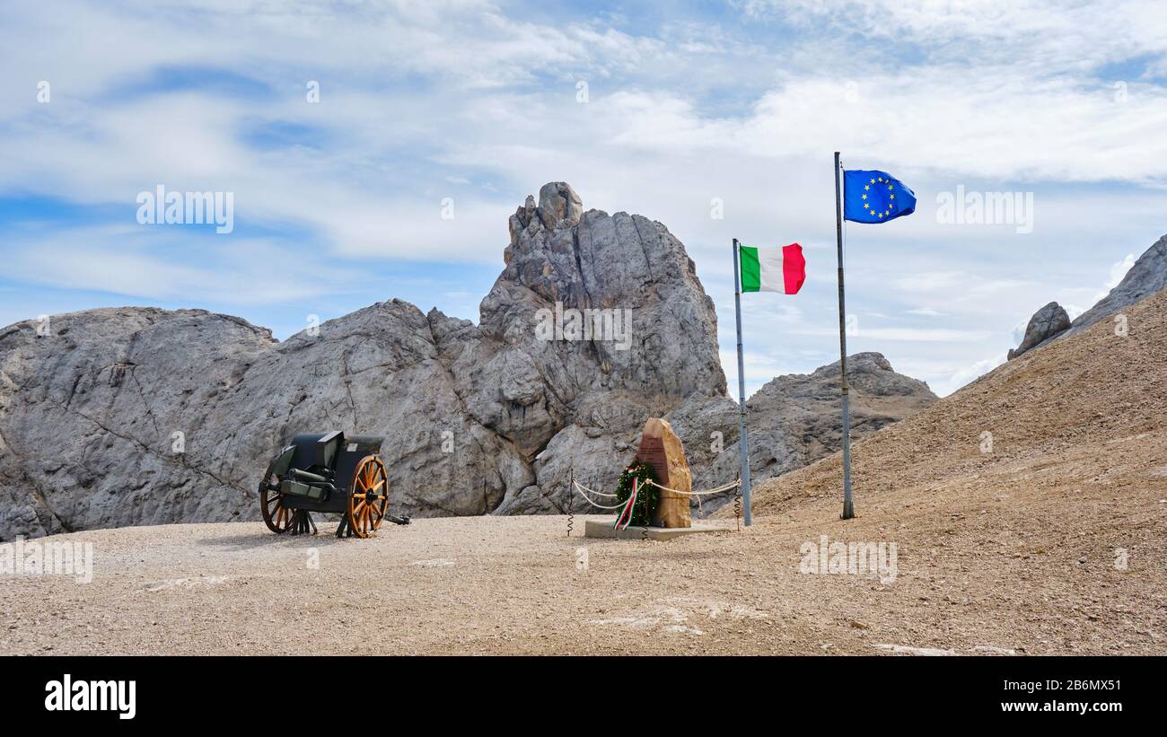 Marmolada, Italia - 28 agosto 2019: Monumento commemorativo della prima guerra mondiale con bandiere italiane ed europee vicino ad un vecchio cannone, a Punta Serauta, ghiacciaio della Marmolada. Foto Stock