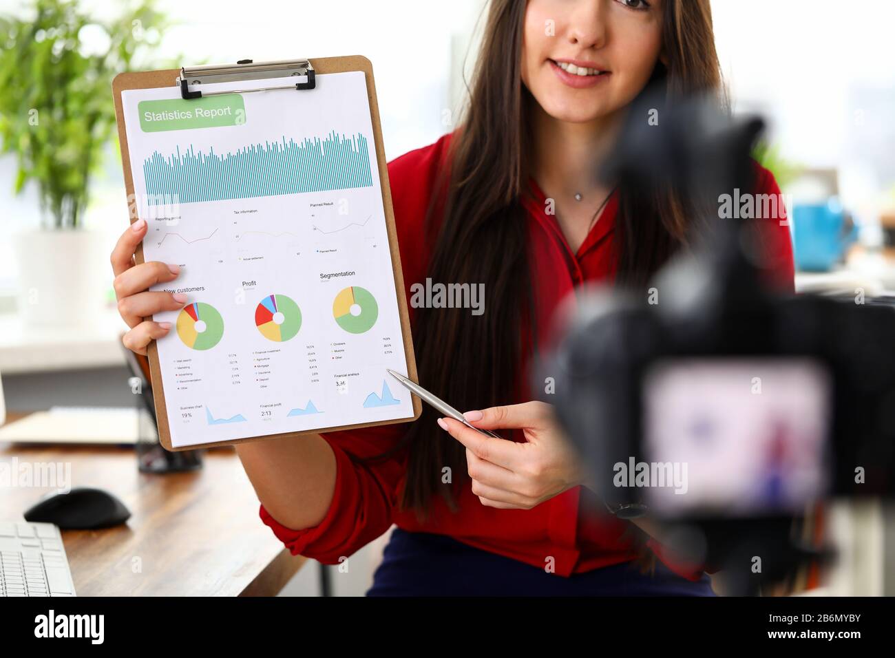 Giovane donna seduto in ufficio di fronte alla telecamera e presentando statistiche e report di analisi. Foto Stock